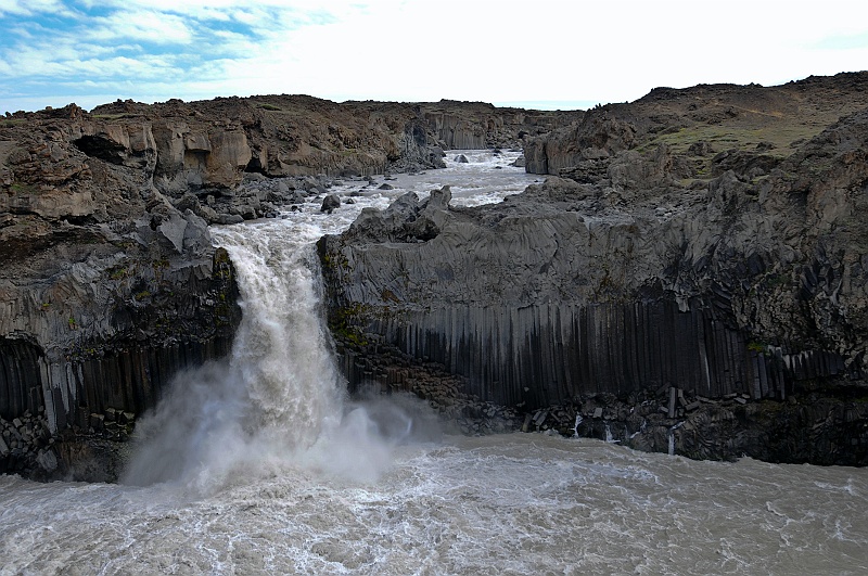 ABC_5770.jpg - Aldeyjarfoss - La coul�e de lave vue en coupe constitue un mod�le parfait de mur d'orgues basaltiques. La s�paration est tr�s nette entre la partie profonde de la lave, qui s'est refroidie assez lentement pour s'organiser en orgues, et la r�gion sup�rieure plus tourment�e qui ne pr�sente que des �bauches de prismation, au point que l'on pourrait croire � deux coul�es distinctes superpos�es. Les colonnades sont toujours orient�es perpendiculairement � la surface par laquelle la lave s'est refroidie, en l'occurrence le sol, ce qui fait qu'elles s'incurvent pour �pouser le relief lorsque la coul�e a but� sur un obstacle.